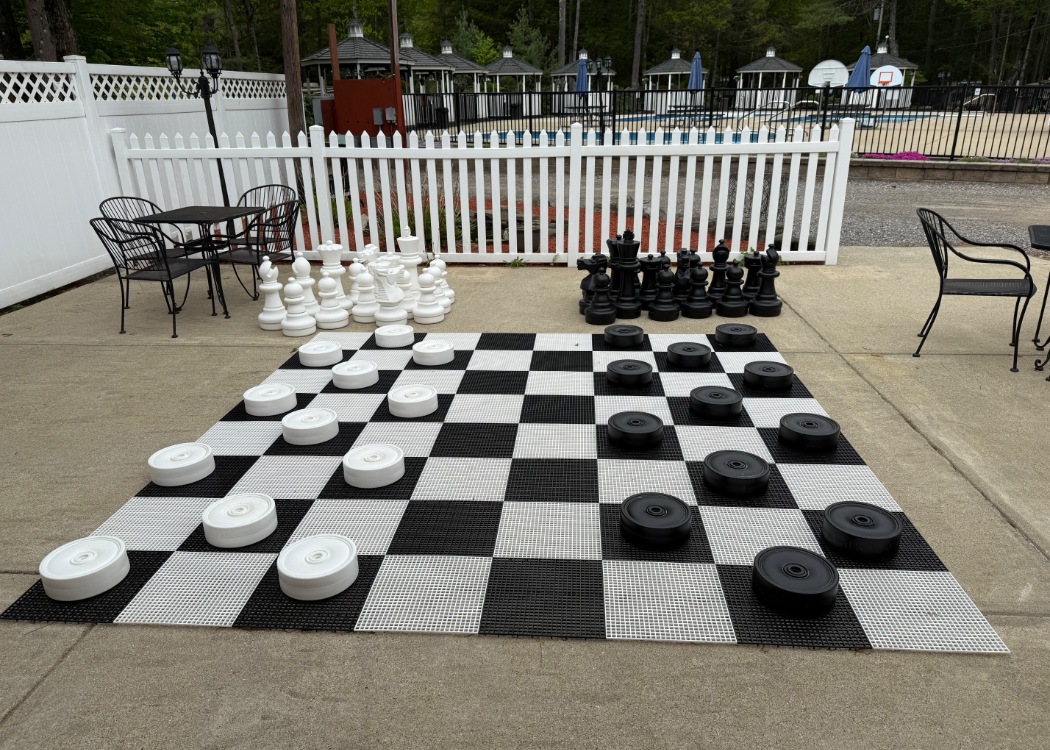 Oversized board with chess and checker pieces outdoor on a patio.